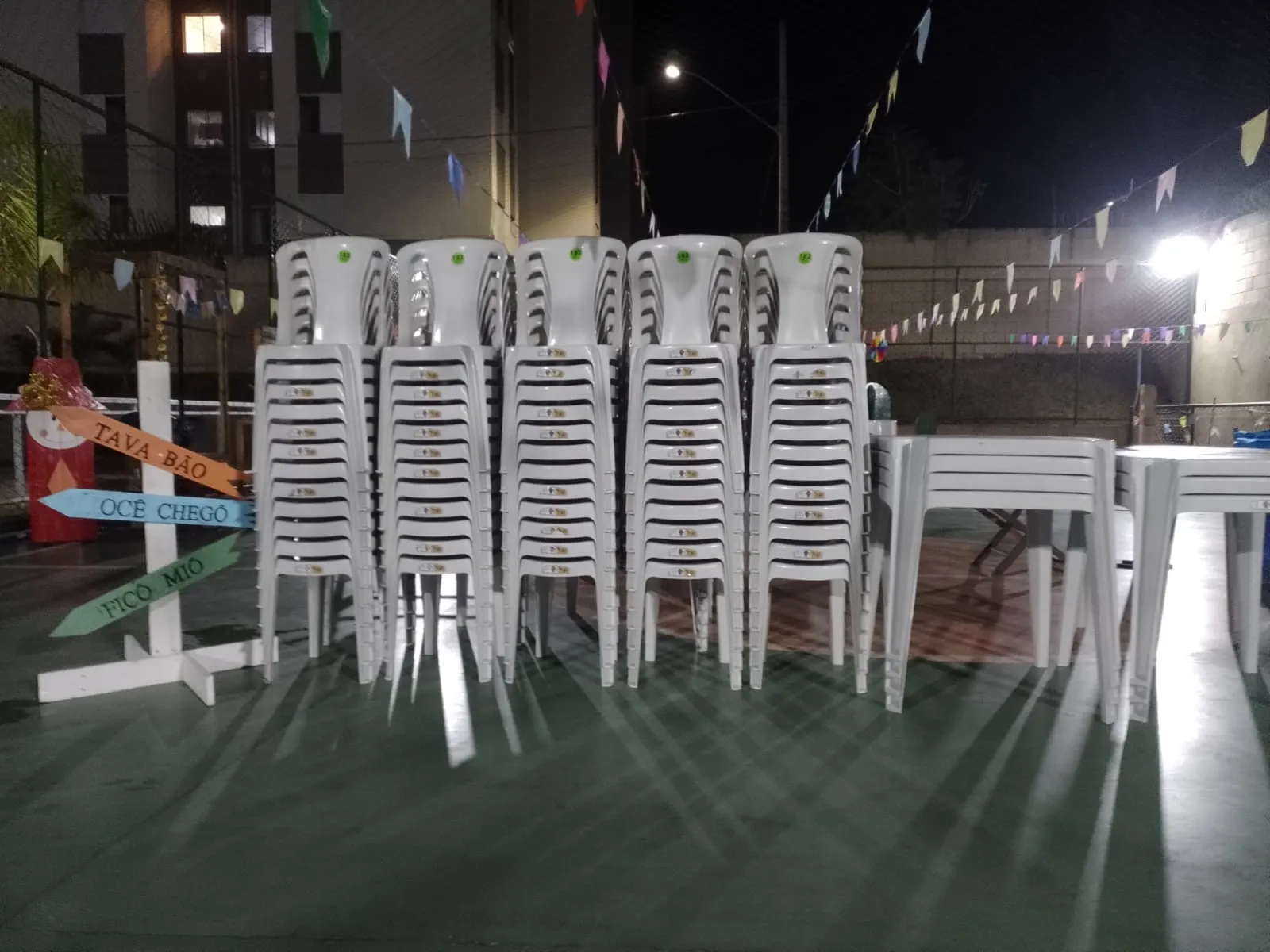 Cadeiras brancas empilhadas prontas para uma festa junina à noite