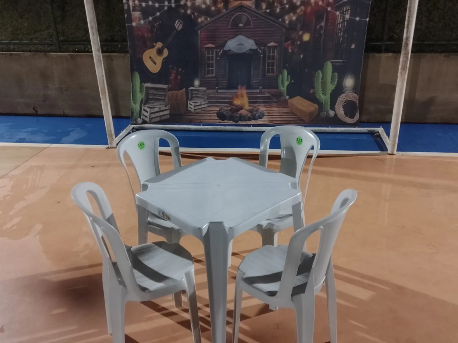 Mesa com quatro cadeiras diante de painel de festa junina