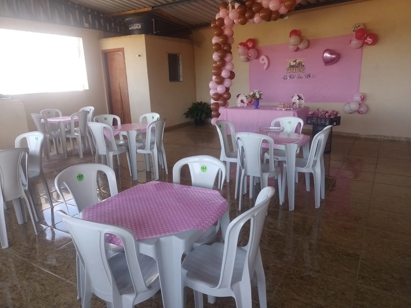 Salão de festas com mesas de toalha rosa e arco de balões